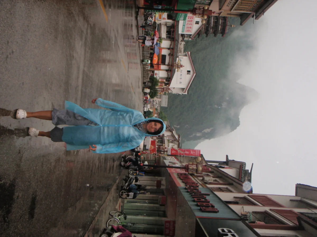 Erika v pršiplášti na daždivej ulici – Yangshuo, Čína