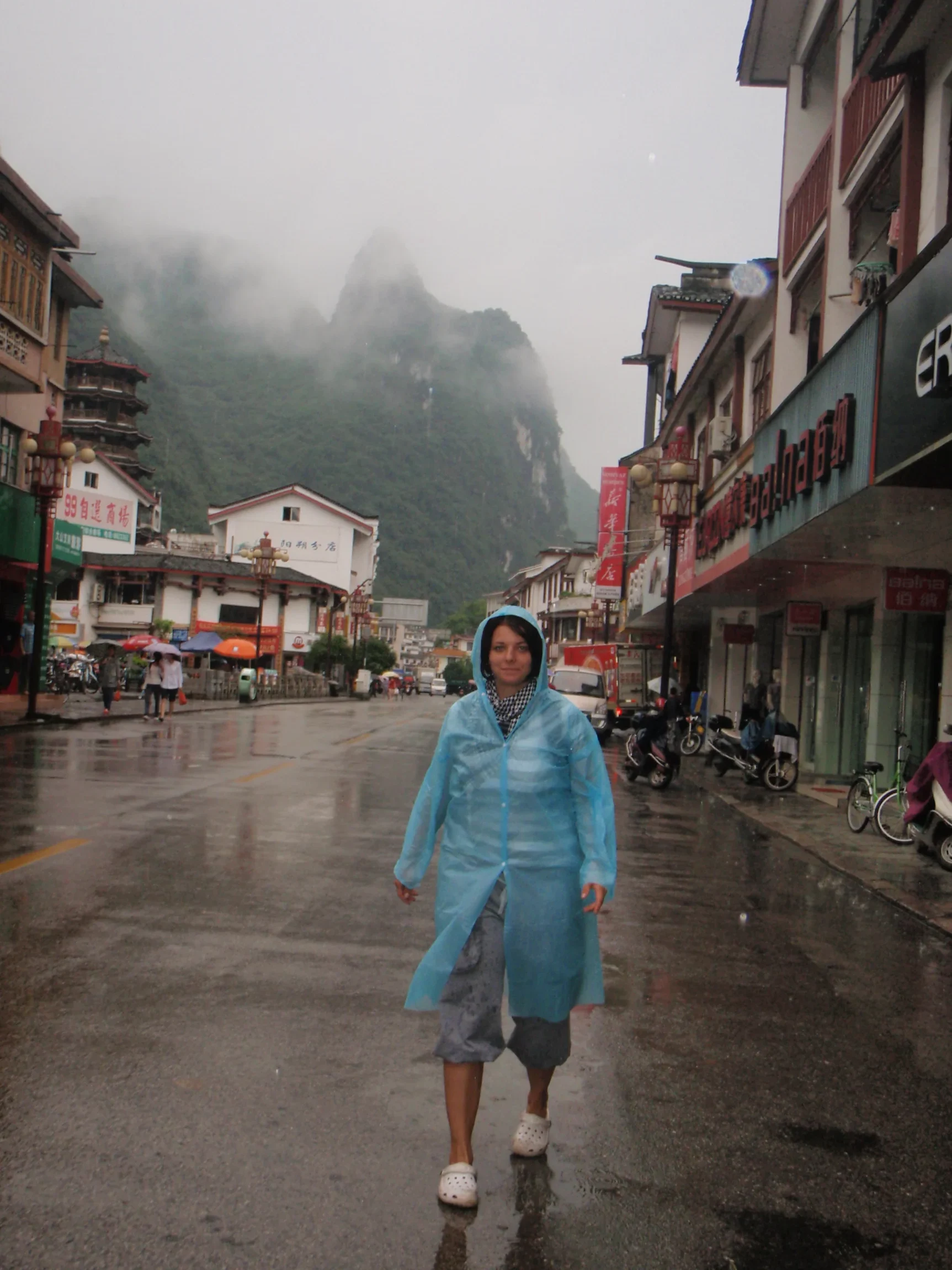 Erika v pršiplášti na daždivej ulici – Yangshuo, Čína
